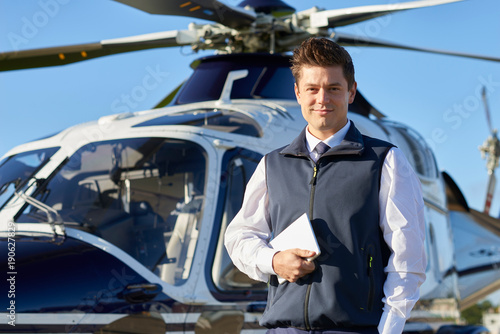 Portrait Of Pilot Standing In Front Of Helicopter With Digital Tablet