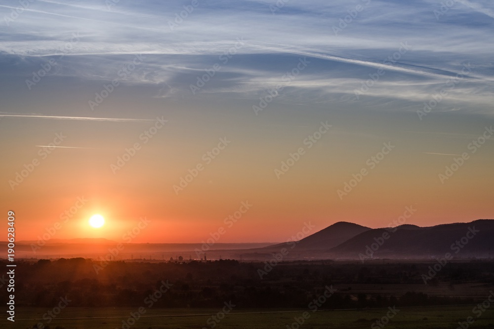 Sunset landscape with colorful sun rays fine clouds and silhouettes of the hills