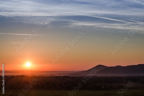 Sunset landscape with colorful sun rays fine clouds and silhouettes of the hills © Gabriel