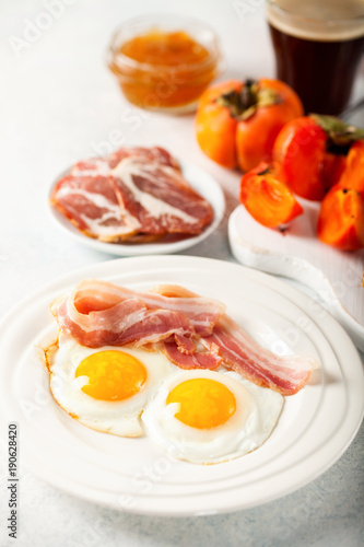 Fried eggs, bacon, a toast, a persimmon