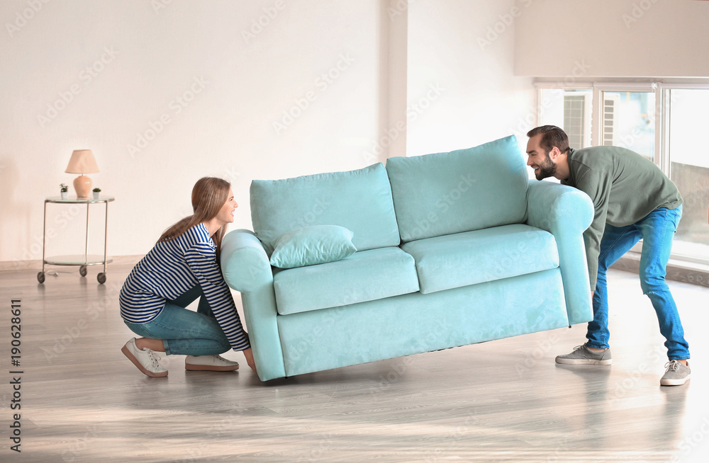 Young couple moving sofa in room at new home