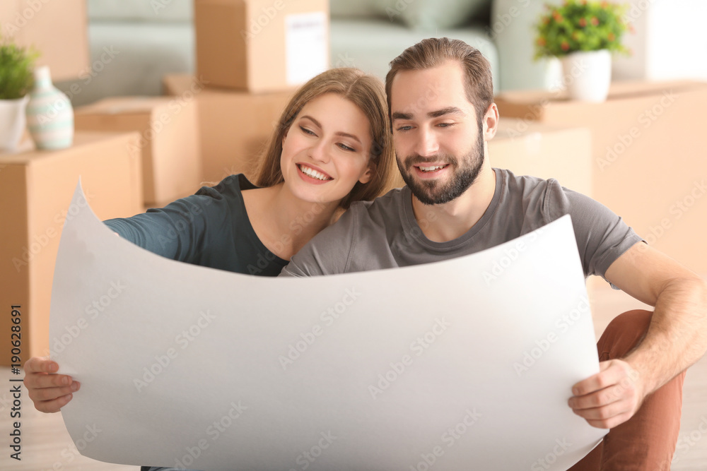 Young couple with house plan sitting on floor after moving to new home