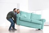 Young couple moving sofa in room at new home