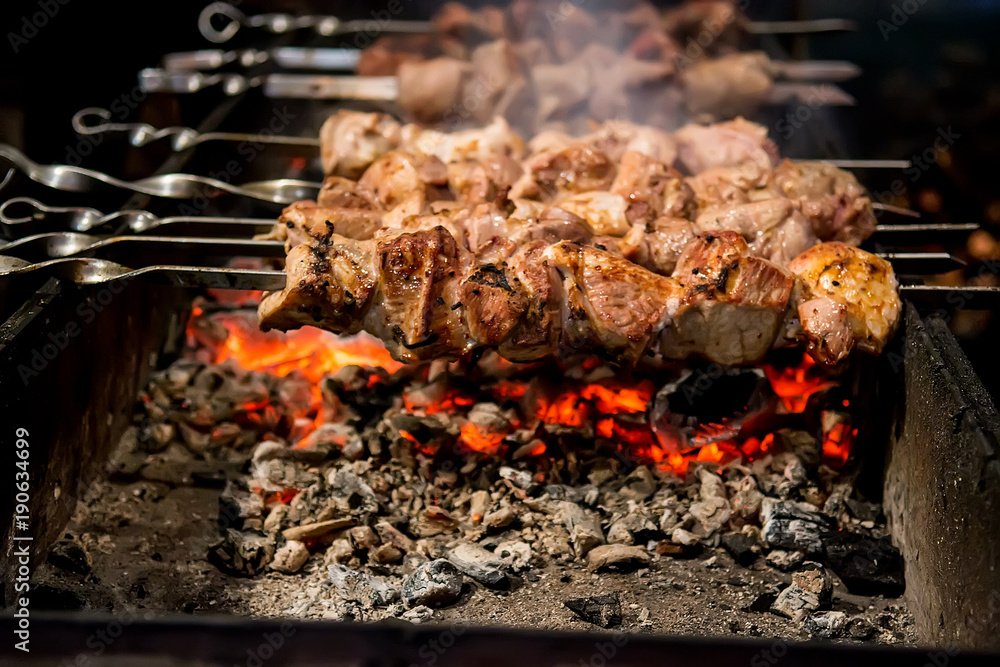 Grilled kebab cooking on metal skewer. BBQ fresh beef meat chop slices. Traditional eastern dish, shish kebab. Grill on charcoal and flame, picnic, street food