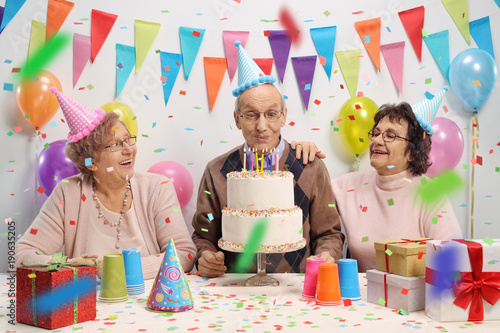 Photography Elderly man with two elderly women blowing candles on a birthday cake
