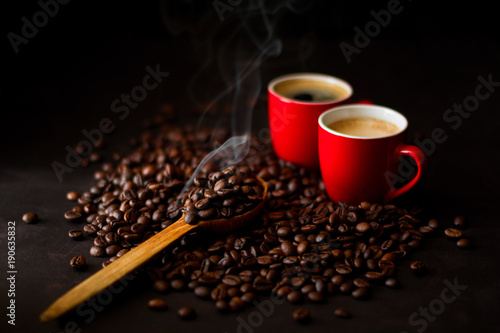 Two red cups of espresso with coffee beans on dark wooden background. Smoke taking away from coffee seeds