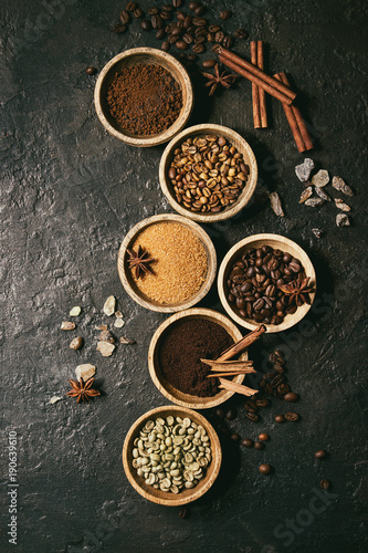 Variety of grounded, instant coffee, different coffee beans, brown sugar, spices in wooden bowls over dark texture background. Top view, space. Toned image