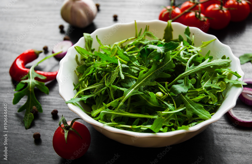 Green rucola fresh salad in white bowl on dark wooden background Green rucola fresh salad in white bowl on dark wooden background