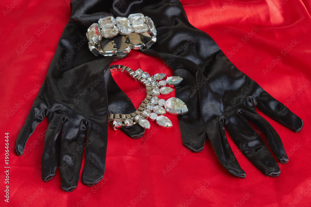 two pretty black gloves next to shiny necklace and bracelet on red background