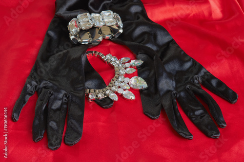 two pretty black gloves next to shiny necklace and bracelet on red background