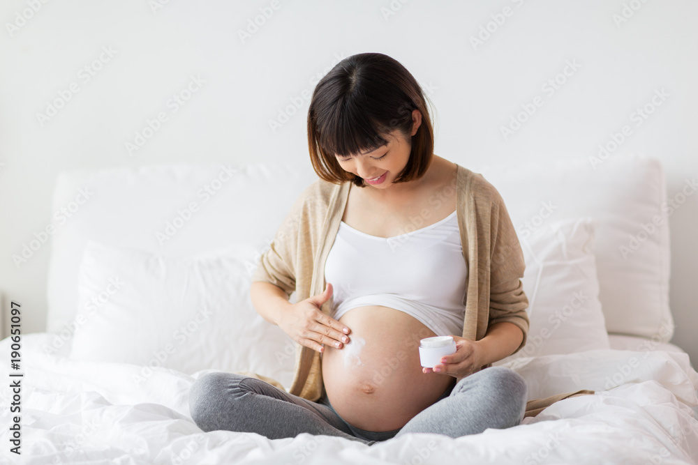 happy asian pregnant woman applying cream to belly