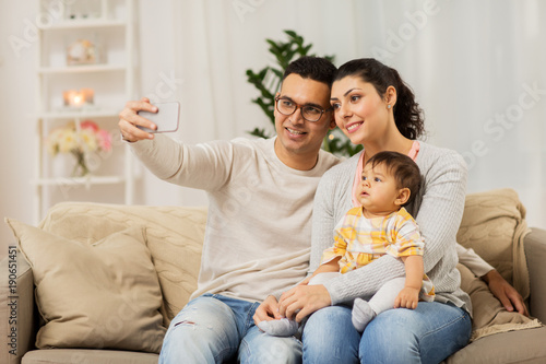 mother and father with baby taking selfie at home
