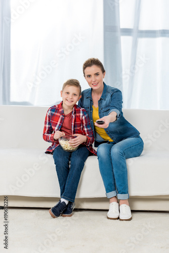 mother and son watching tv together with popcorn on couch