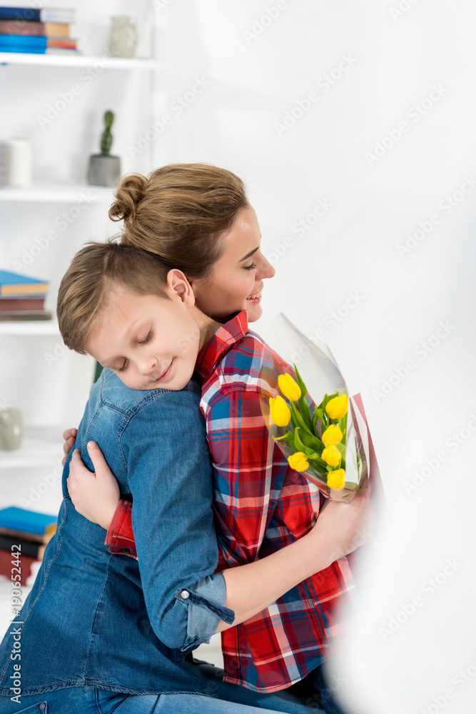Fototapeta premium mother and son embracing on mothers day after he gave her flowers