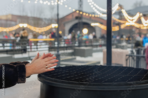 woman warming his hands at the big iron stove in the background of a skating rink in winter Park
