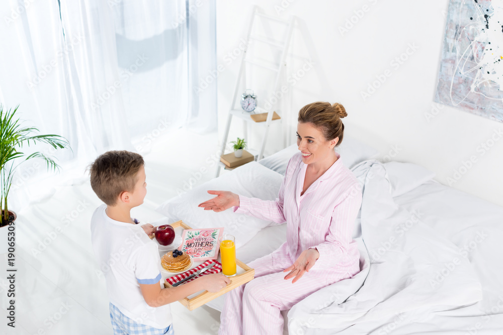 high angle view of son carrying breakfast for mother while she sitting on bed