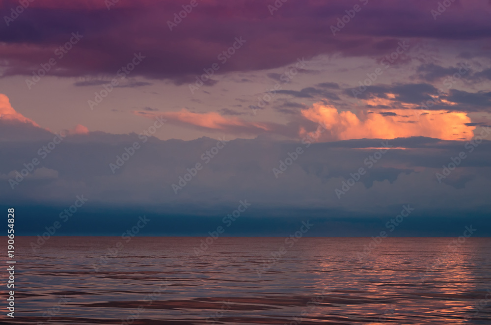 large storm clouds on the Azov Sea, illuminated by the setting sun, the sea horizon. Reflection on the water surface.