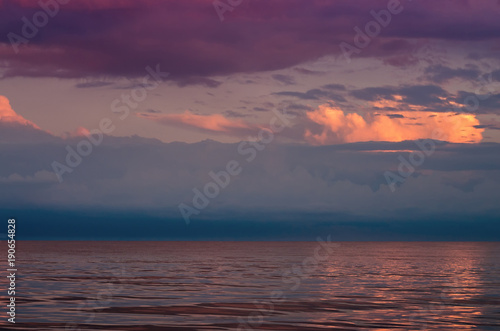 large storm clouds on the Azov Sea, illuminated by the setting sun, the sea horizon. Reflection on the water surface. © balakleypb