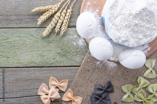 Spike of wheat, pasta, eggs and flour on a wooden background, with space for text photo