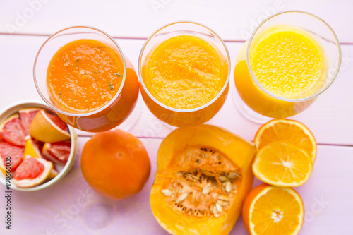 Healthy Food, Diet Concept. Three glasses of fruit and vegetable smoothie in a raw with pieces of fresh orange, pumpkin and grapefruit on pink wooden background, top view