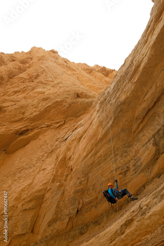 Female climber abseiling down from rock cliff in dry wadi in Judea desert.