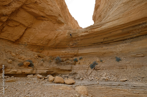 Climber abseiling down from rock cliff in dry wadi in Judea desert.
