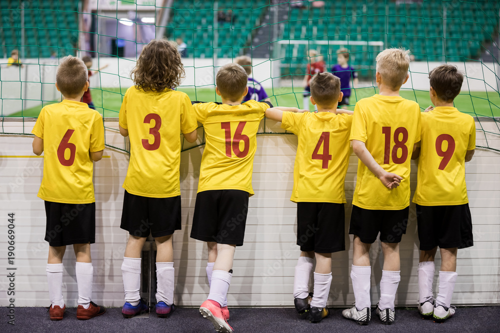 Obraz premium Indoor soccer team. Futsal indoor soccer match for kids. Children supporting teammates. Sports arena in the background. Indoor football school tournament for kids