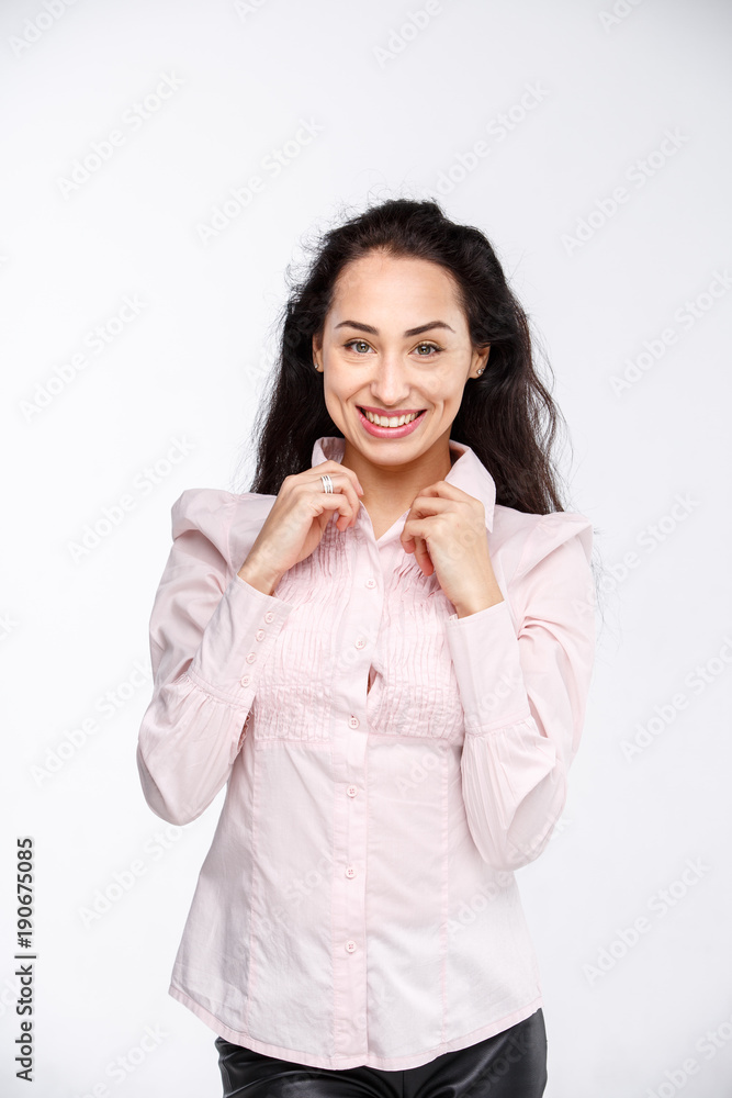 Portrait of a young beautiful caucasian woman with long black hair in a pink shirt is holding hands on a collar on a light background in the studio Portrait of a young beautiful caucasian woman with long black hair in a pink shirt is holding hands on a collar on a light background in the studio