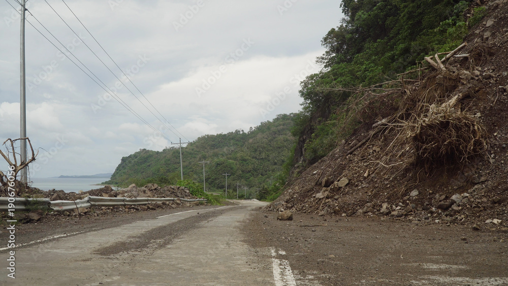 Naklejka premium Landslides and rockfalls on the road in the mountains. Mud and rocks blocking the road.Destroyed rural road landslide damaged in powerful flood. Collapsed on the mountain. Philippines, Camiguin.
