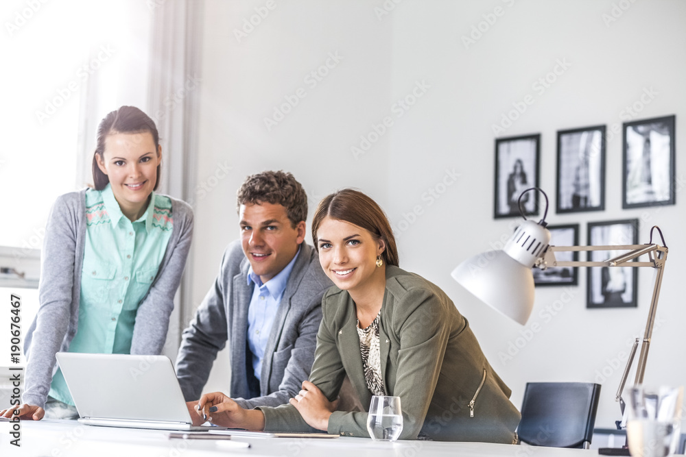 Obraz premium Portrait of smiling young business people with laptop at desk in office