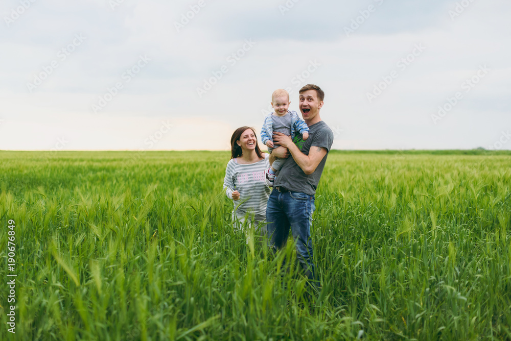 Joyful man, woman walk on green field background, rest, have fun, play, stand with little cute child baby boy. Mother, father, little kid son. Family day 15 of may, love, parents, children concept. Joyful man, woman walk on green field background, rest, have fun, play, stand with little cute child baby boy. Mother, father, little kid son. Family day 15 of may, love, parents, children concept.