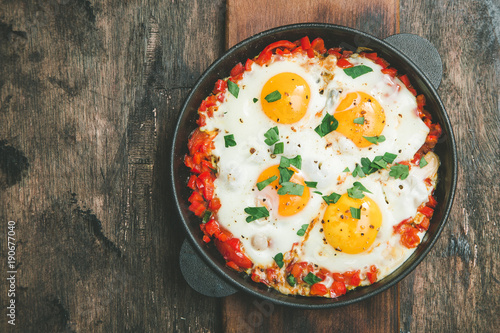 Tasty and Healthy Shakshuka in a Frying Pan. Fried eggs with tomatoes, bell pepper, vegetables and herbs. Middle eastern traditional dish.