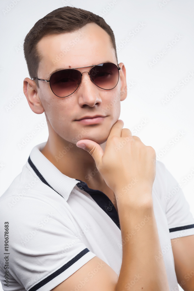 A young positive man in sunglasses, lit by warm sunlight. Emotional, courageous face. Isolated on white background. Copy space. A young positive man in sunglasses, lit by warm sunlight. Emotional, courageous face. Isolated on white background. Copy space.