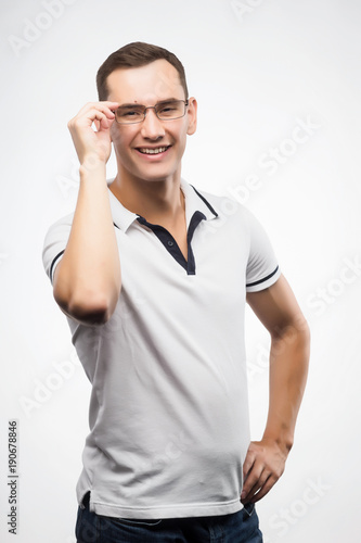 A young positive man in eyeglasses straightens his glasses with his hand. Emotional, courageous face. Isolated on white background. Copy space.