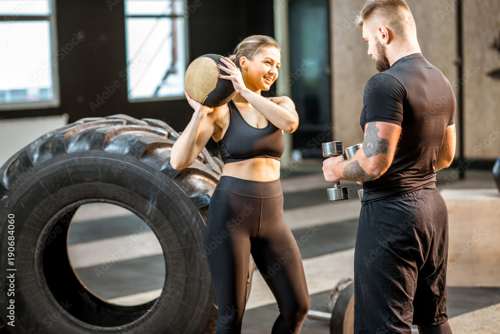 Young athletic couple talking together standing with weights and ball in the crossfit gym