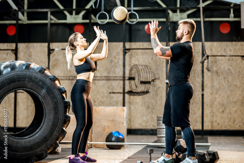 Young athletic couple in blacksportswear training with crossfit wall ball in the gym photo