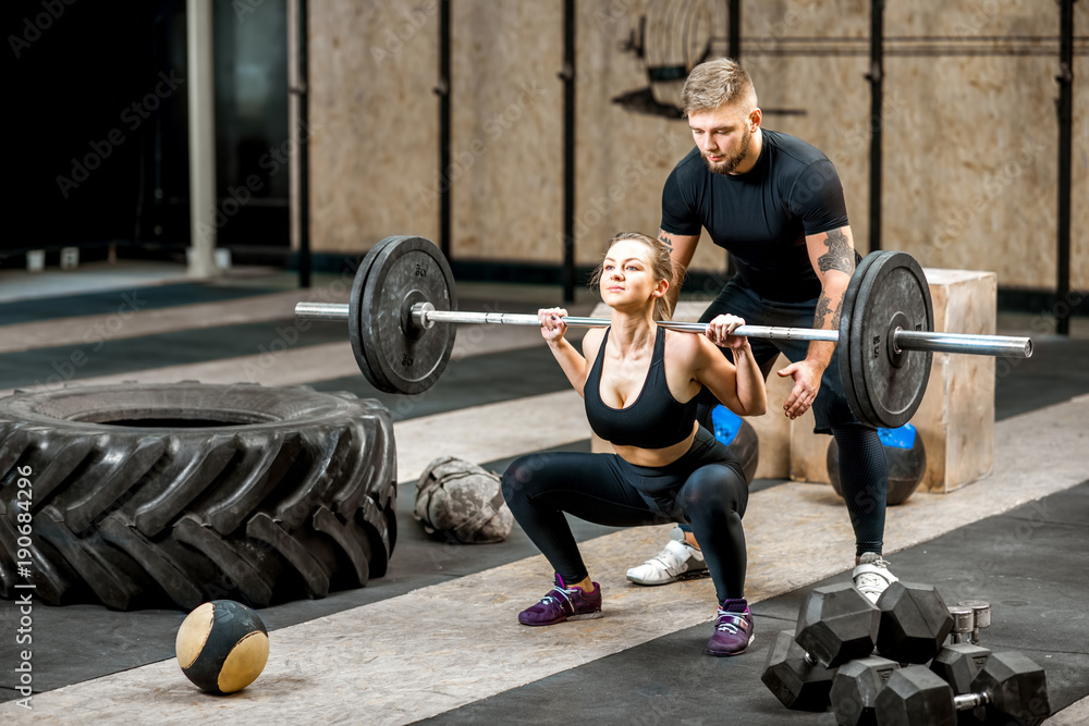 Young athletic woman lifting up the burbell with the help of a coach in the  crossfit gym Stock Photo | Adobe Stock