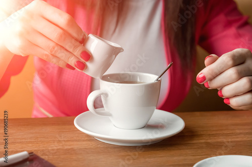 Close-up  hands of a young girl  pours cream or milk into coffee in a cafe on a wooden table.