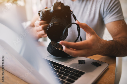 Man taking off lens of a professional camera while using a laptop.