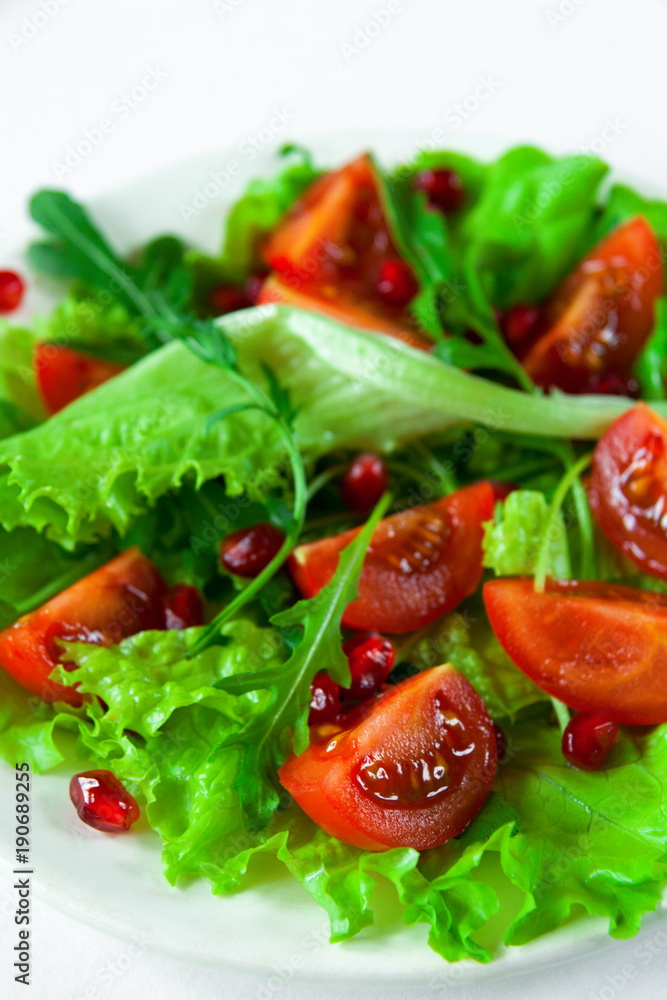 Salad on a white plate on a white background. Cherry tomatoes, arugula and pomegranate seeds on fresh lettuce leaves. Close-up. Salad on a white plate on a white background. Cherry tomatoes, arugula and pomegranate seeds on fresh lettuce leaves. Close-up.