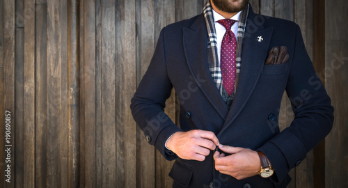 Tableau sur toile Suited man buttoning his coat and posing in front of wooden background