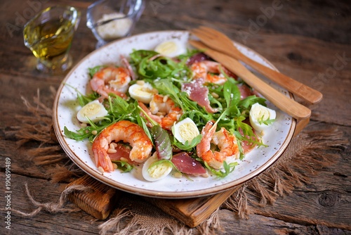 Healthy salad with shrimps, arugula, Parma ham, quail eggs and parmesan cheese.