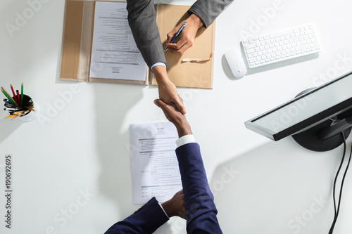 Businessperson Shaking Hand With Candidate Over White Desk