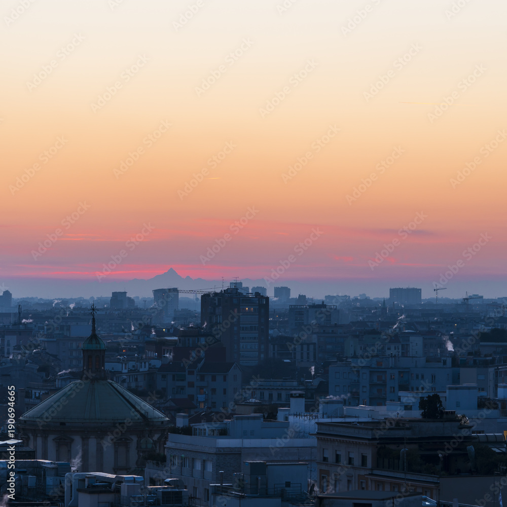 Milan (Italy) cityscape at sunset with the Monviso mountain on the background. Italian cityscape.