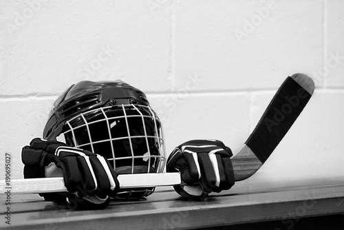 Black and white photo of hockey equipment on the bench: Helmet, gloves and stick