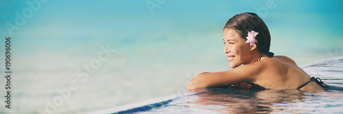 Luxury resort swimming pool Asian woman tourist relaxing in holiday retreat on summer travel vacation. Bikini girl in sunbathing swimsuit enjoying ocean background. Panorama banner.