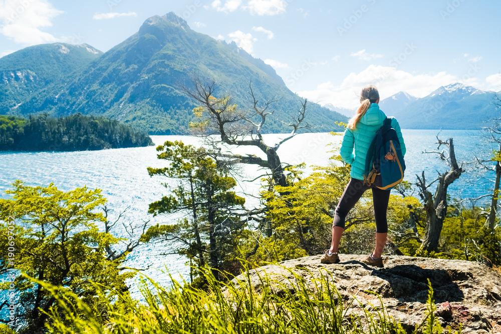 Naklejka premium Woman hiker stands on the coast of the lake and enjoys mountain view. Lake district of Argentina