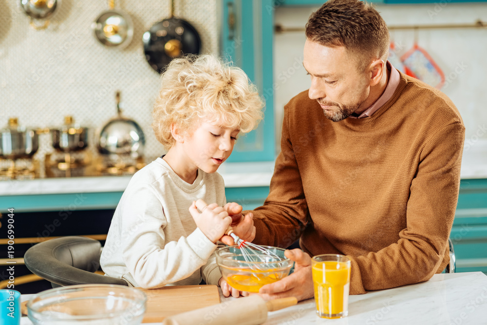 Time together. Pleasant nice good looking man holding his sons hand and trying to help him to cook while spending time together Time together. Pleasant nice good looking man holding his sons hand and trying to help him to cook while spending time together