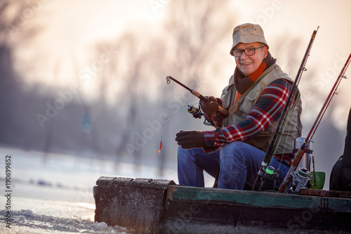 portrait of fisherman with fishing rod sit on frozen river in the winter