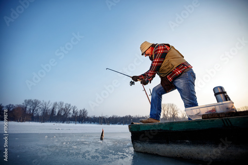 Smiling fisherman catch fish on the frozen river in winter